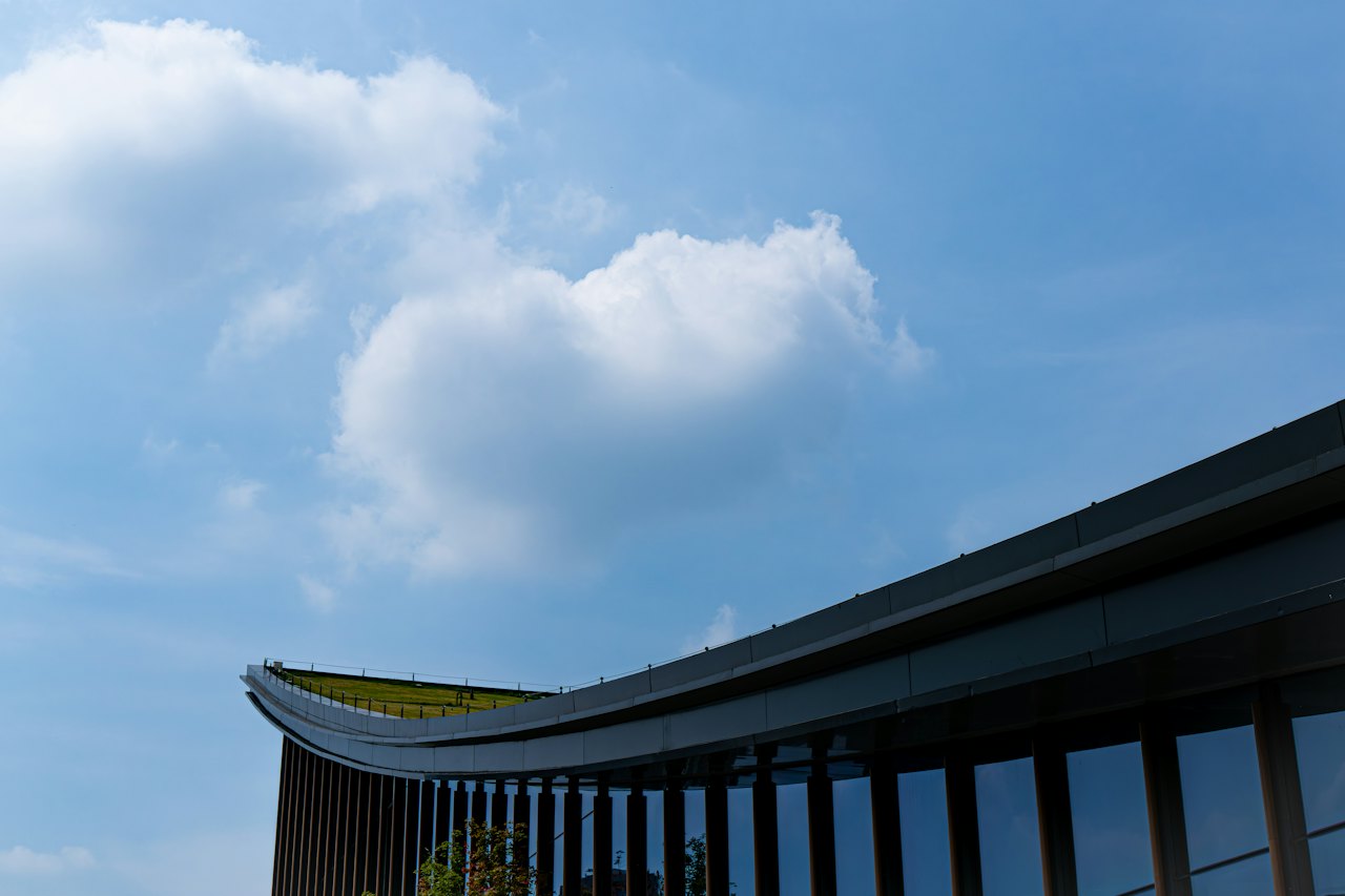 A curved building roof against a bright sky with clouds